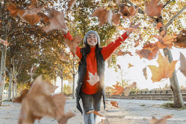 Playful young woman throwing autumn leaves on footpath - JRVF02530