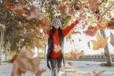 Verspielte junge Frau, die Herbstblätter auf den Fußweg wirft - JRVF02530