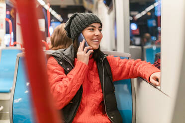 Glückliche junge Frau, die telefoniert und durch ein Straßenbahnfenster hinausschaut - JRVF02536