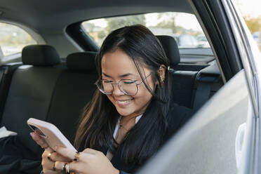 Lächelnde Geschäftsfrau mit Smartphone auf dem Rücksitz eines Autos - JRVF02581