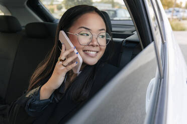 Geschäftsfrau schaut aus dem Autofenster und spricht mit ihrem Smartphone - JRVF02582