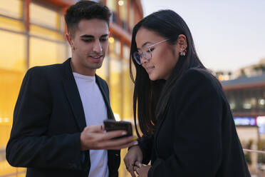 Businessman showing smart phone to businesswoman in city - JRVF02587