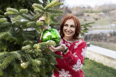 Lächelnde Frau hängt Weihnachtsschmuck an den Baum - JCCMF05207