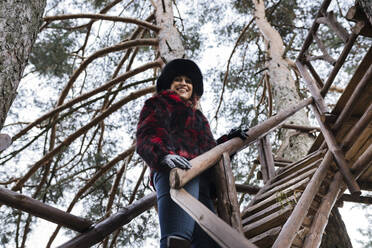 Smiling woman on tree house steps in forest - JCCMF05231