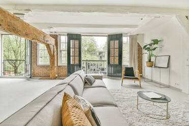 Geräumige helle Studio Interieur mit weißen Wänden mit bequemen Sofa auf Teppich in der Nähe von Couchtisch und Sessel und offene Tür und mit Pflanzen dekoriert platziert - ADSF33248