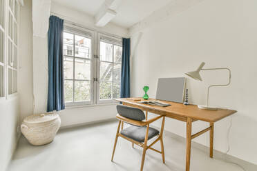 Modern interior of spacious room furnished with wooden table and armchair placed near window in light apartment - ADSF33254