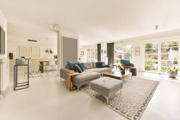 Cozy gray sofa and armchair with poufs and coffee table placed in spacious living room near dining zone in modern apartment decorated with framed pictures in daylight - ADSF33308