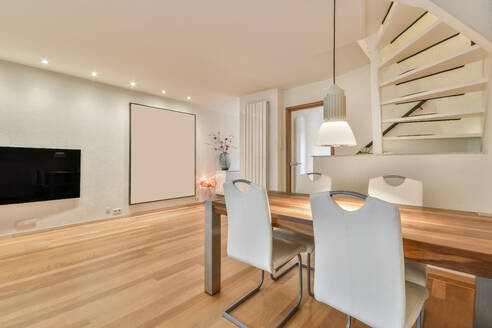 Interieur eines modernen Wohnzimmers mit Laminatboden und Essecke mit Tisch und Stühlen sowie einer beleuchteten Hängelampe - ADSF33340