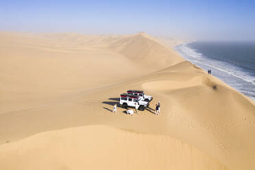 Luftaufnahme von Menschen bei einem Fotoshooting auf den Sanddünen entlang der Küstenlinie in der Nähe von Walvis Bay, Namibia. - AAEF13632