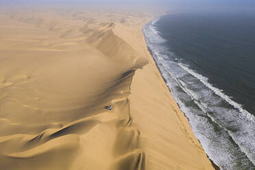 Luftaufnahme von zwei Geländewagen, die auf den Sanddünen entlang der Küstenlinie in der Nähe von Walvis Bay, Namibia, geparkt sind. - AAEF13640