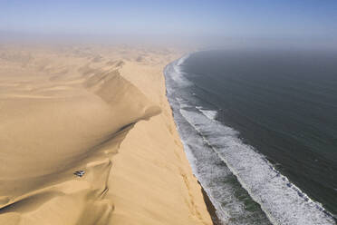 Luftaufnahme von zwei Geländewagen, die auf den Sanddünen entlang der Küstenlinie in der Nähe von Walvis Bay, Namibia, geparkt sind. - AAEF13641