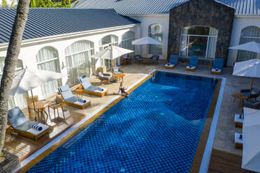Luftaufnahme einer schönen Frau, die sich in einem Luxushotel mit Swimmingpool entspannt, Pointe de Flacq, Mauritius. - AAEF13812