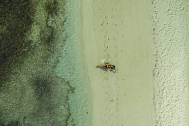 Luftaufnahme einer Frau, die sich am Ufer eines paradiesischen Strandes auf der Ile aux Cerfs entspannt, einer kleinen Insel in der Nähe der Küstenlinie und des Riffs, Mauritius. - AAEF13839