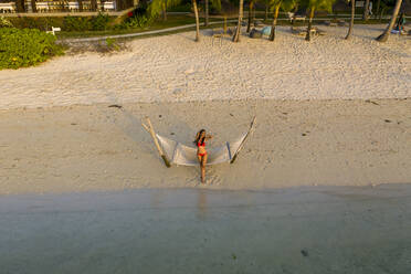 Aerial view of a beautiful attractive woman relaxing on a hammock along the beach at sunset, Le Morne, Mauritius. - AAEF13845