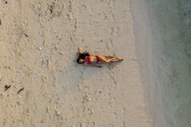 Aerial view of a beautiful attractive woman relaxing on the beach at sunset, Le Morne, Mauritius. - AAEF13847