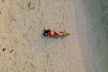 Luftaufnahme einer schönen, attraktiven Frau, die sich bei Sonnenuntergang am Strand entspannt, Le Morne, Mauritius. - AAEF13847