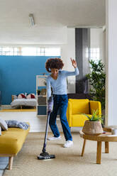 Fröhliche junge Afro-Frau, die Musik genießt und den Teppich im Wohnzimmer reinigt - GIOF14703
