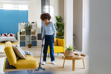 Smiling young woman cleaning carpet in living room - GIOF14704