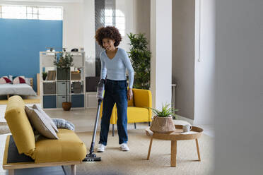 Smiling young Afro woman cleaning carpet in living room - GIOF14705
