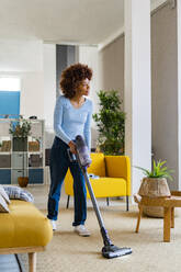 Young Afro woman cleaning carpet in living room at home - GIOF14707