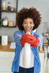 Fröhliche junge Afro-Frau mit Desinfektionssprayflasche in der Küche - GIOF14720