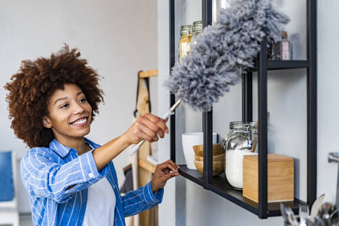 Smiling young woman cleaning rack in kitchen at home - GIOF14736