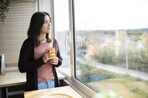 Frau mit Tasse, die aus dem Fenster schaut und zu Hause steht - XLGF02522