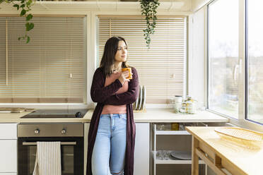 Woman with mug leaning on kitchen counter at home - XLGF02523