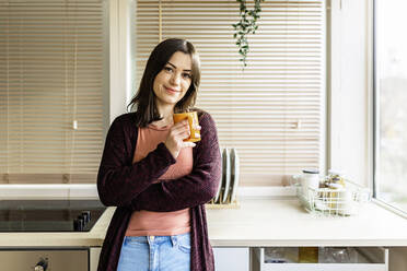 Lächelnde junge Frau hält Tasse in der Küche zu Hause - XLGF02524