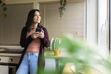 Thoughtful woman with smart phone in kitchen at home - XLGF02526