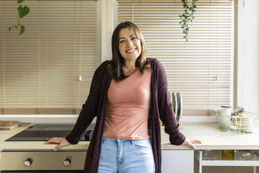 Happy woman leaning on kitchen counter at home - XLGF02538