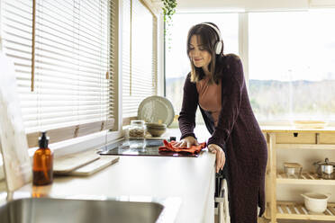 Frau hört Musik beim Reinigen des Induktionsherds in der Küche zu Hause - XLGF02540