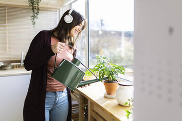 Woman listening music watering houseplant through can at home - XLGF02541