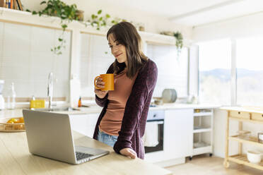 Freiberufler mit Tasse vor Laptop in der Küche zu Hause - XLGF02546