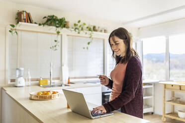 Businesswoman doing online shopping on laptop holding credit card in kitchen at home - XLGF02557