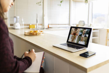 Junge berufstätige Frau mit Notebook bei einem Videogespräch mit Kollegen auf einem Laptop zu Hause - XLGF02565