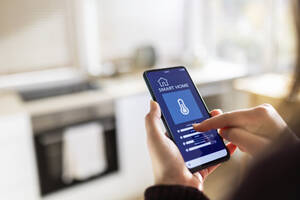 Frau, die zu Hause eine Smart-Home-Anwendung auf ihrem Mobiltelefon nutzt - XLGF02571