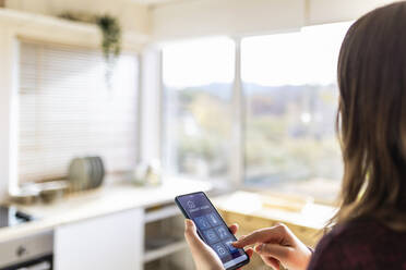 Junge Frau, die eine Smart-Home-Anwendung zu Hause nutzt - XLGF02573