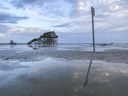 Deutschland, Schleswig-Holstein, Sankt Peter-Ording, Pfützen am Sandstrand in der Sommerdämmerung mit Stelzenhaus im Hintergrund - ASCF01638