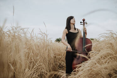 Nachdenkliche Frau mit Cello im Feld stehend - GMLF01221