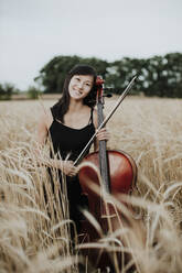 Lächelnde Frau hält Cello inmitten von Feldfrüchten - GMLF01225