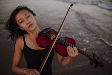 Woman playing violin in sea at beach - GMLF01232