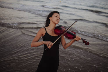 Woman playing violin standing in sea - GMLF01233