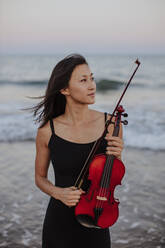Contemplative woman with violin at beach - GMLF01235
