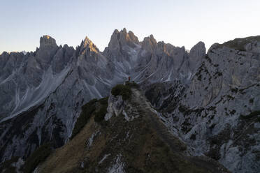 Aerial view of a hiker climbing a mountain crest with Three peaks of Lavaredo in background, Dolomites, Italy. - AAEF13865