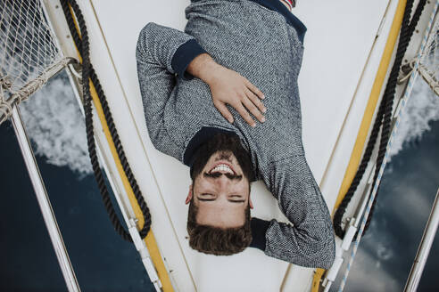 Lächelnder junger Mann auf Segelboot liegend - GMLF01236