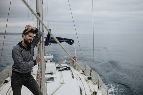 Thoughtful man leaning on mast of sailboat in Mediterranean Sea - GMLF01237