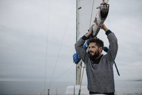 Nachdenklicher junger Mann lehnt am Mast eines Segelboots im Mittelmeer - GMLF01239