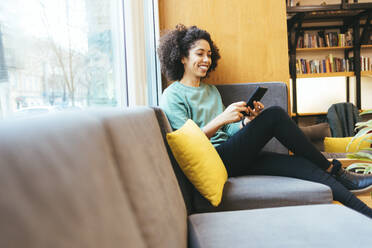 Smiling businesswoman using smart phone on sofa - OYF00644