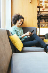 Glückliche Geschäftsfrau, die auf dem Sofa eine Textnachricht auf ihrem Smartphone schreibt - OYF00647